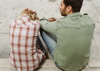A couple sitting on concrete steps with their backs to the camera; the woman appears distressed, holding her head in her hands, while the man looks away thoughtfully,Your Personality Sabotaging Your Relationships